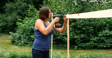 Woman in blue shirt building a trellis outside in garden.