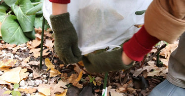 Bag of old garden contents being closed up by hands wearing mittens.