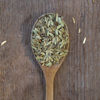 Whole, pale green fennel seed on a rustic wooden spoon.