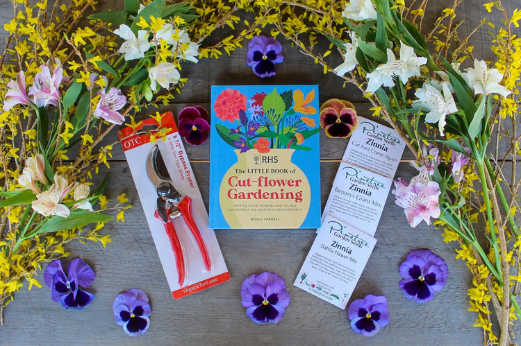 Garden tools, a flower gardening book, and pansies arranged with yellow forsythia branches and white lilies.