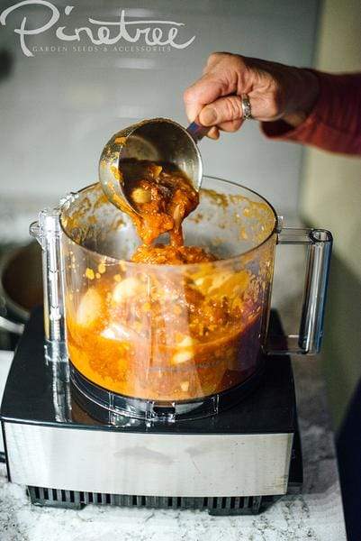 hand pouring chunky sauce from a measuring cup into food processor on kitchen counter