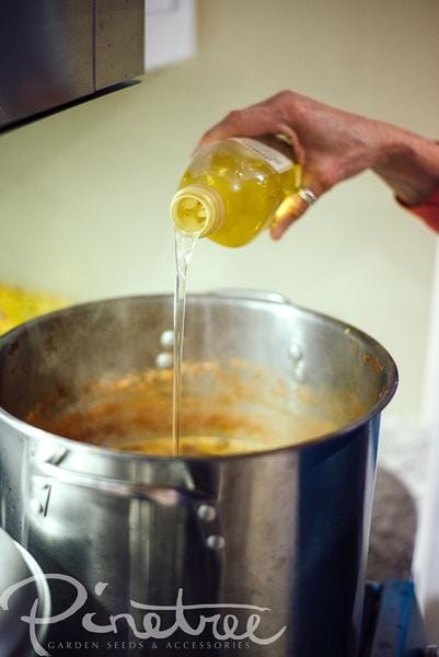 hand pouring olive oil from a bottle into a pot with sauce on stove