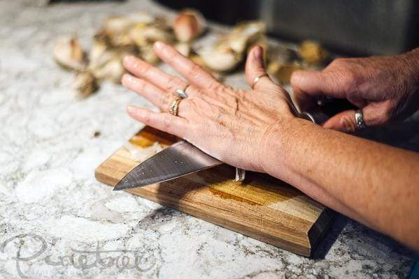 smashing garlic with a knife on a cutting board in the kitchen