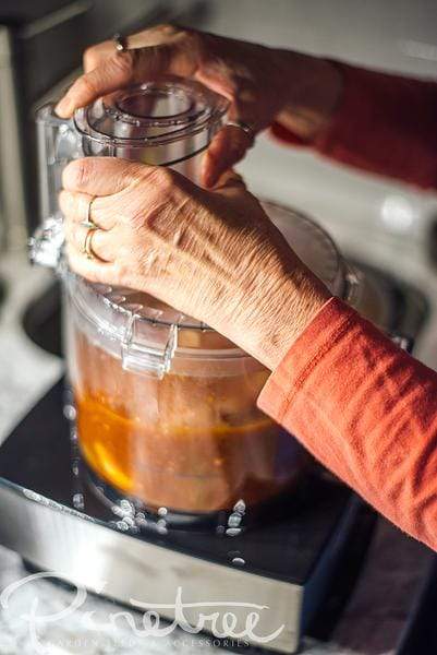 food processor on kitchen counter with sauce and hands closing top