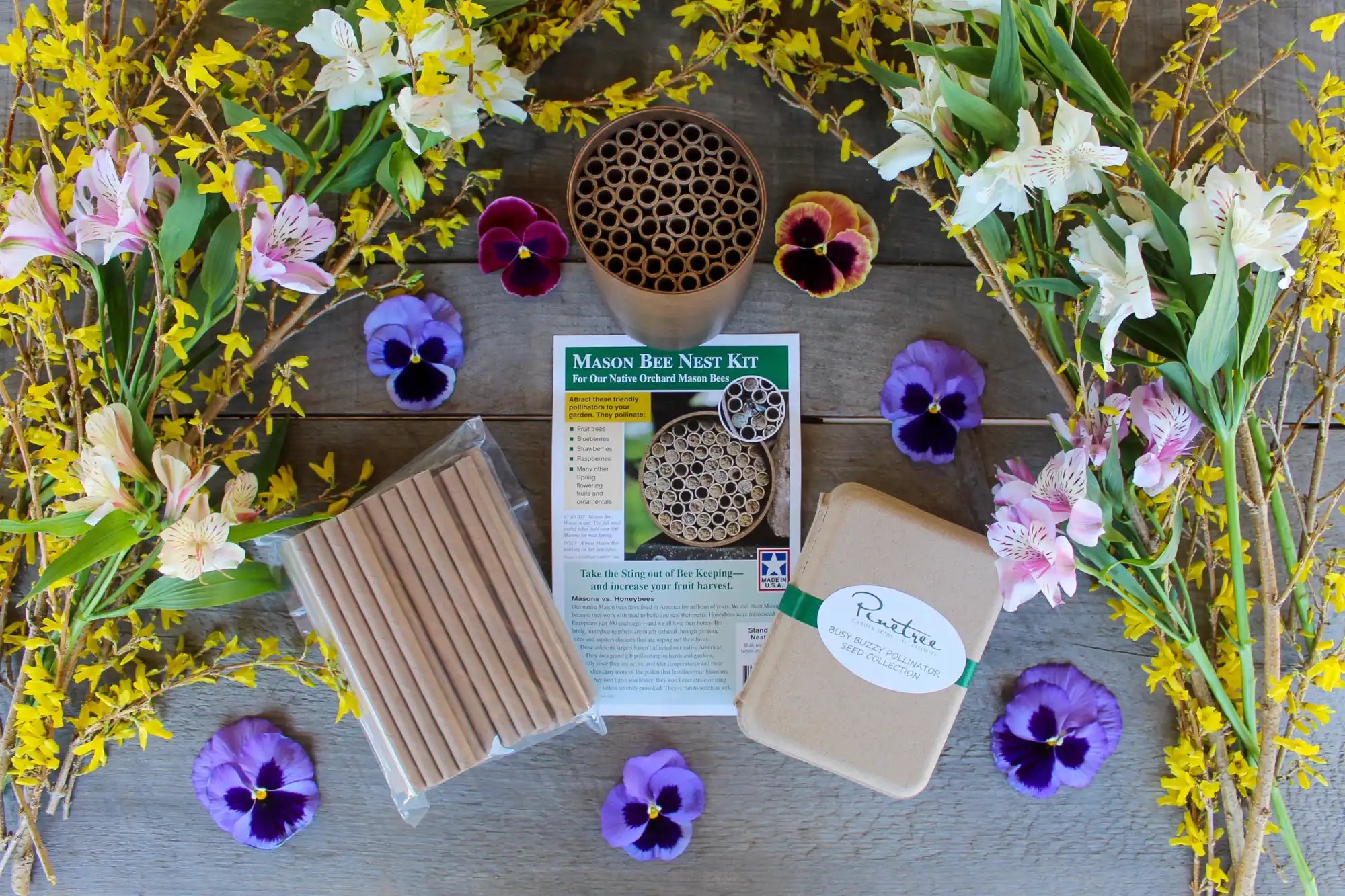 Mason bee house kit with bamboo tubes and colorful pansies arranged around it.