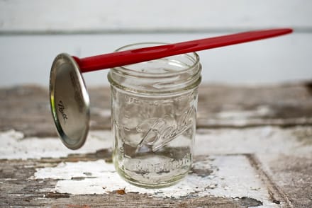 Red canning tool used to lift can lids and remove bubbles attached to a mason jar.