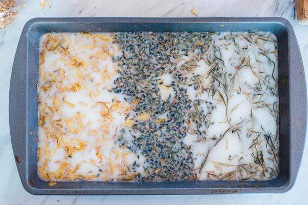 Garden herbs being mixed into soap in a baking pan.