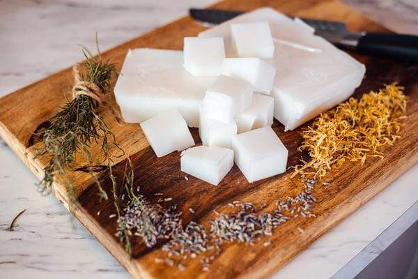 Soap bases and homegrown herbs on a wooden cutting board.