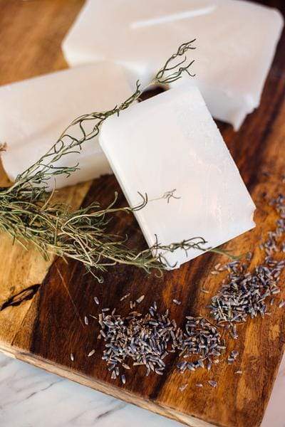 Soap base bars and home grown herbs on a wooden cutting board.