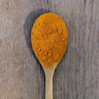 Bright orange turmeric powder on wooder spoon.